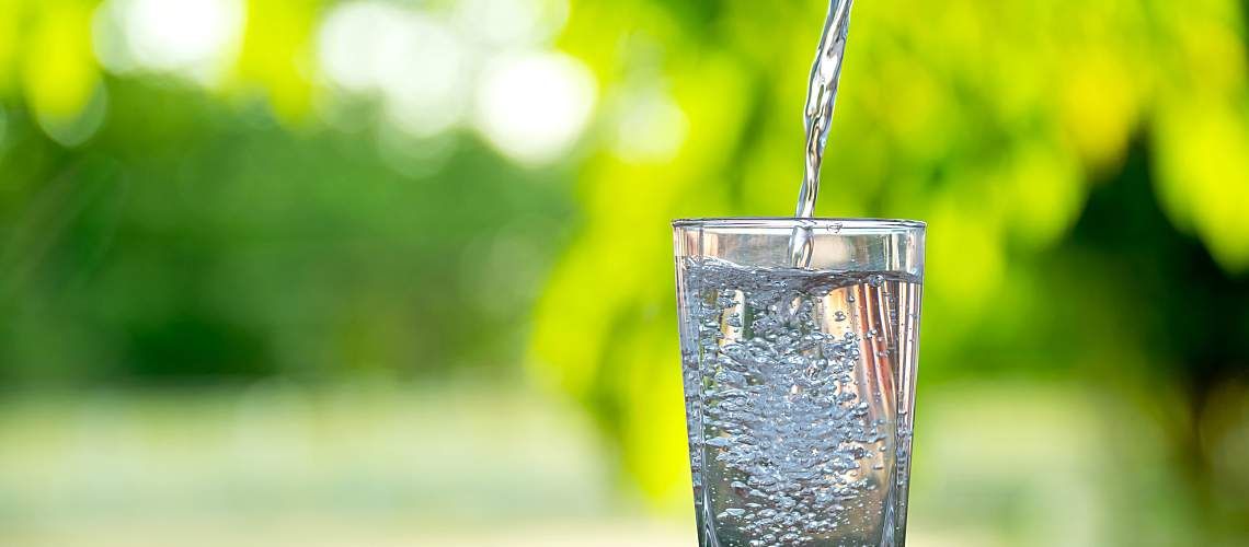 A narrow stream of water is poured into a tall glass.