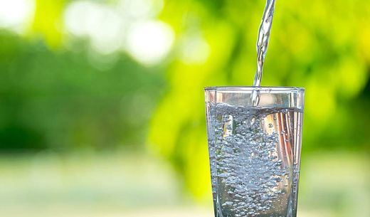 A narrow stream of water is poured into a tall glass.