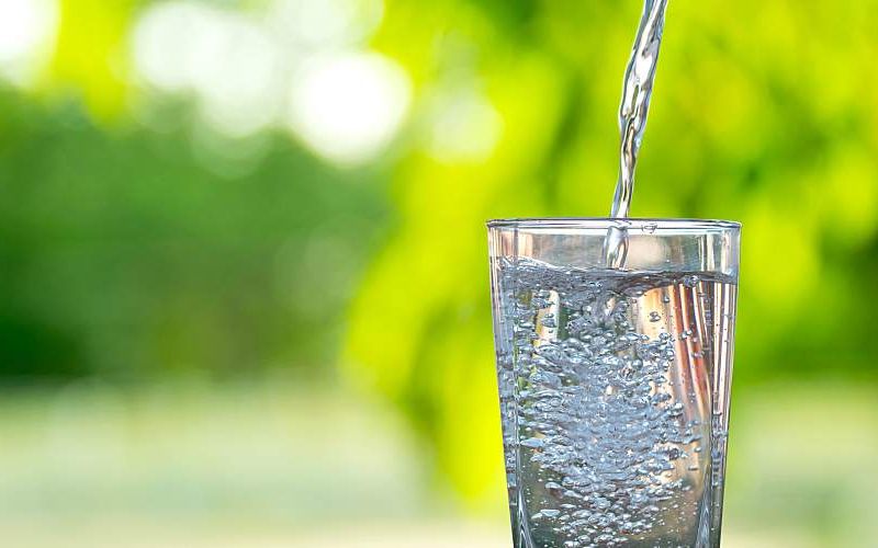 A narrow stream of water is poured into a tall glass.