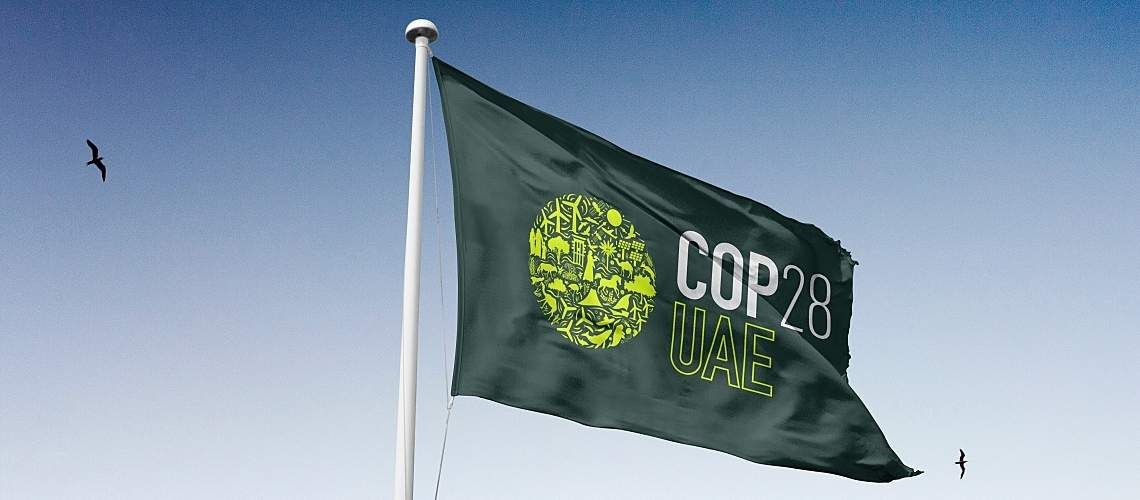 A green COP28 flag against a blue sky.
