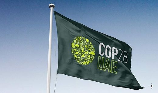 A green COP28 flag against a blue sky.