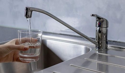 A person fills a clear glass with water running from the sink.