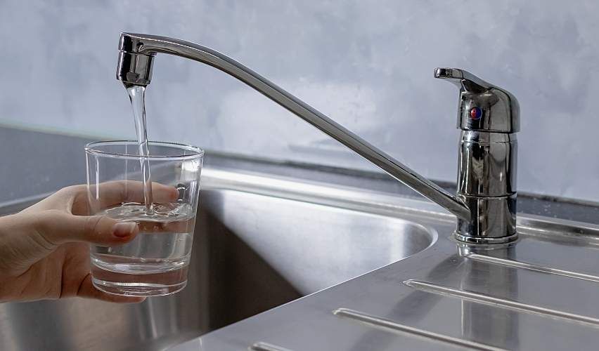 A person fills a clear glass with water running from the sink.