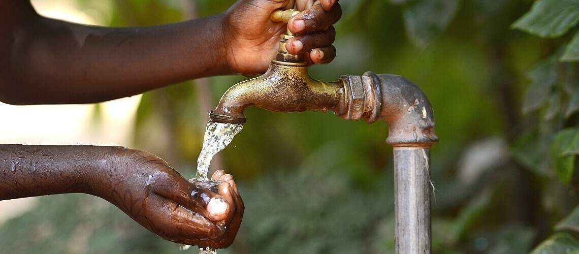 An African child turns on an outdoor tap.