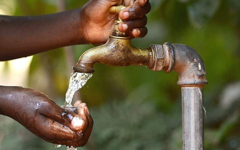 An African child turns on an outdoor tap.