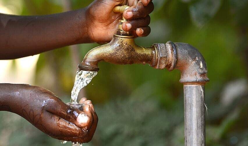 An African child turns on an outdoor tap.