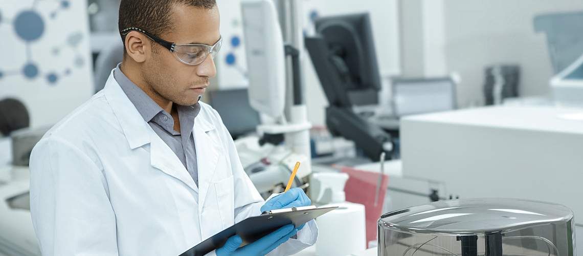 A researcher in a lab writes on a clipboard.