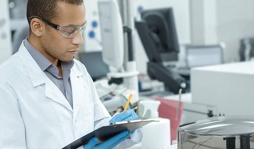 A researcher in a lab writes on a clipboard.