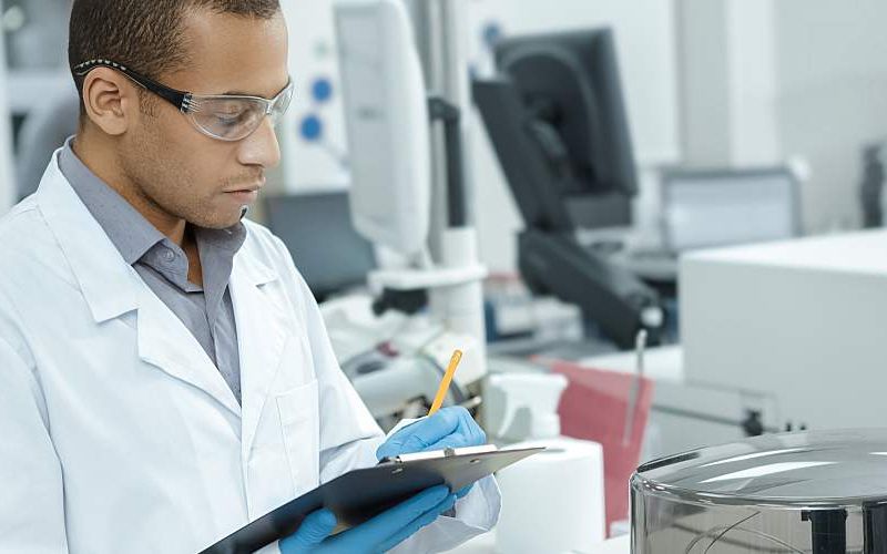 A researcher in a lab writes on a clipboard.