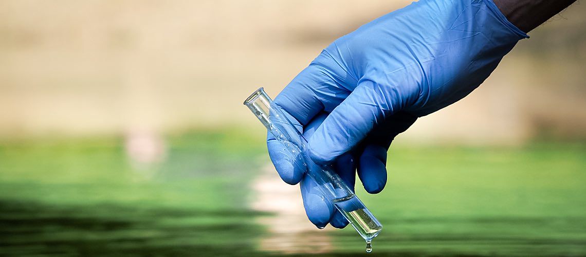 A hand in a latex glove holds a beaker.