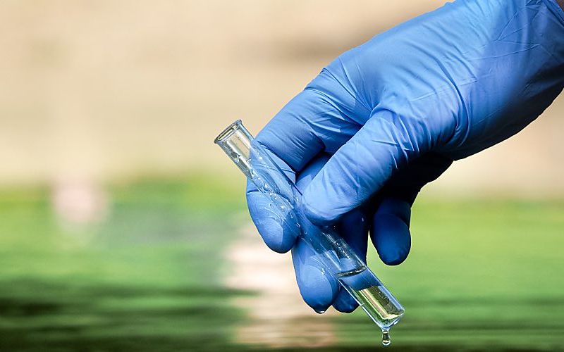 A hand in a latex glove holds a beaker.