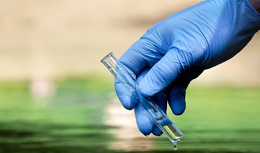 A hand in a latex glove holds a beaker.