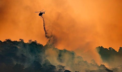 A helicopter drops water on a forest fire.