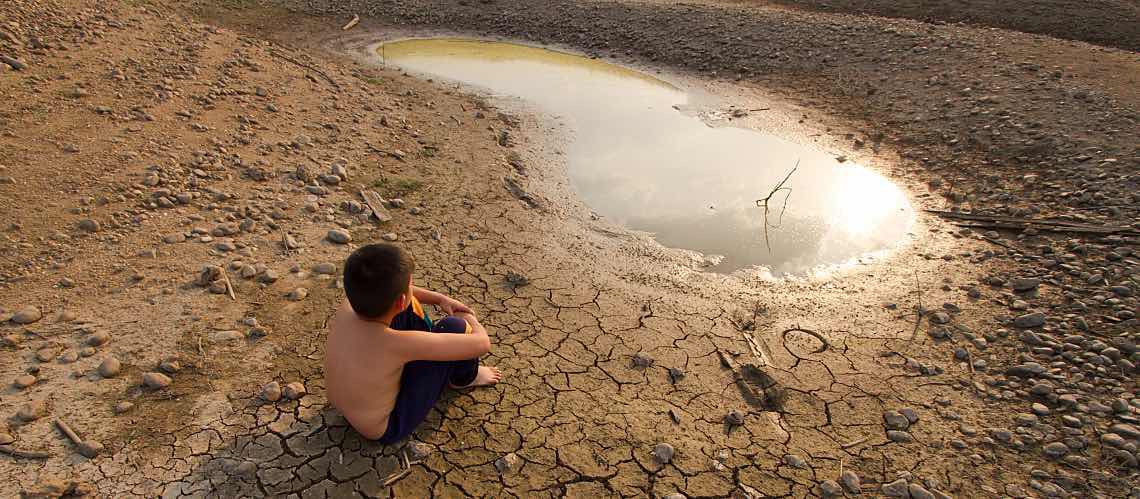 Boy sits on cracked earth by small puddle of water