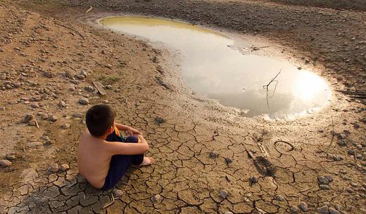 Boy sits on cracked earth by small puddle of water