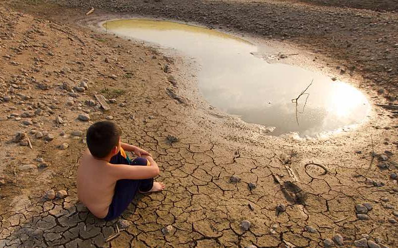 Boy sits on cracked earth by small puddle of water