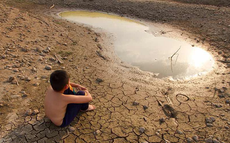 Boy sits on cracked earth by small puddle of water