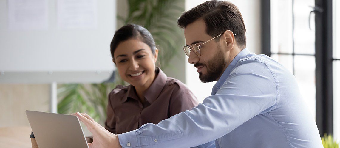 A man and woman look at a laptop screen.