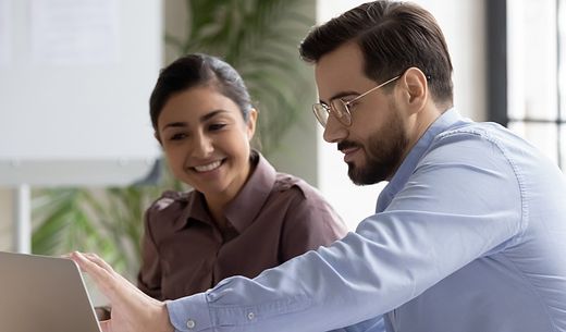 A man and woman look at a laptop screen.