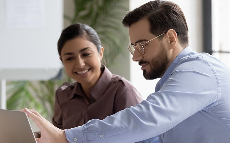 A man and woman look at a laptop screen.