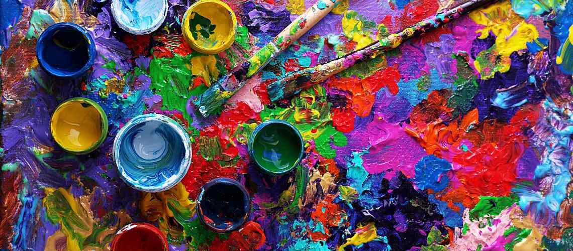 Mix of colorful paints with bottles and brushes on an artist pad.