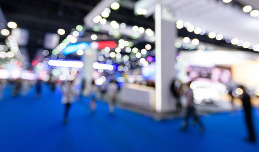 A blurred image of exhibitor booths at a trade show.