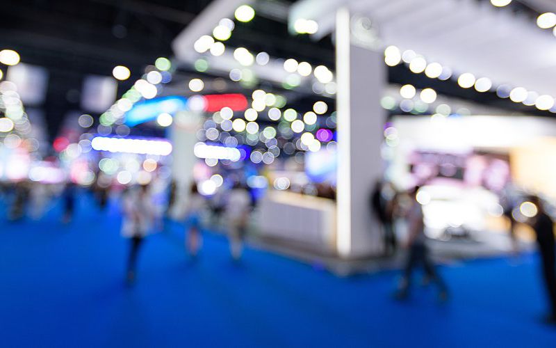 A blurred image of exhibitor booths at a trade show.