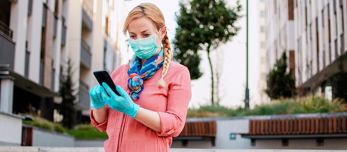 Woman looks at phone wearing mask and protective gloves.