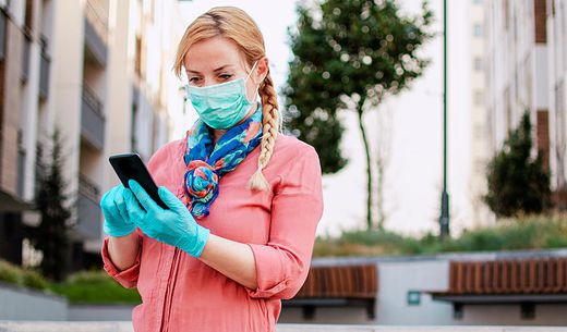 Woman looks at phone wearing mask and protective gloves.