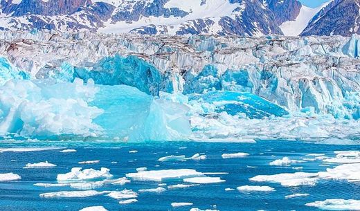 A glacier surrounded by blue water with floating ice.