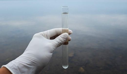 A person's hand in a plastic glove holds a water sample.