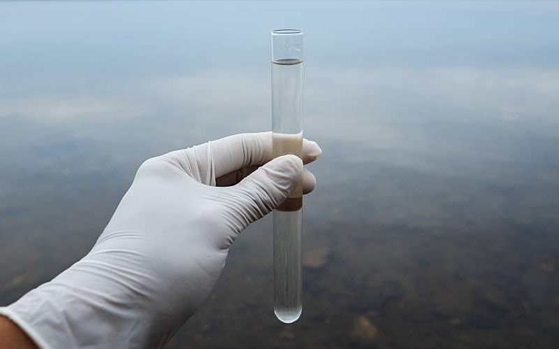 A person's hand in a plastic glove holds a water sample.