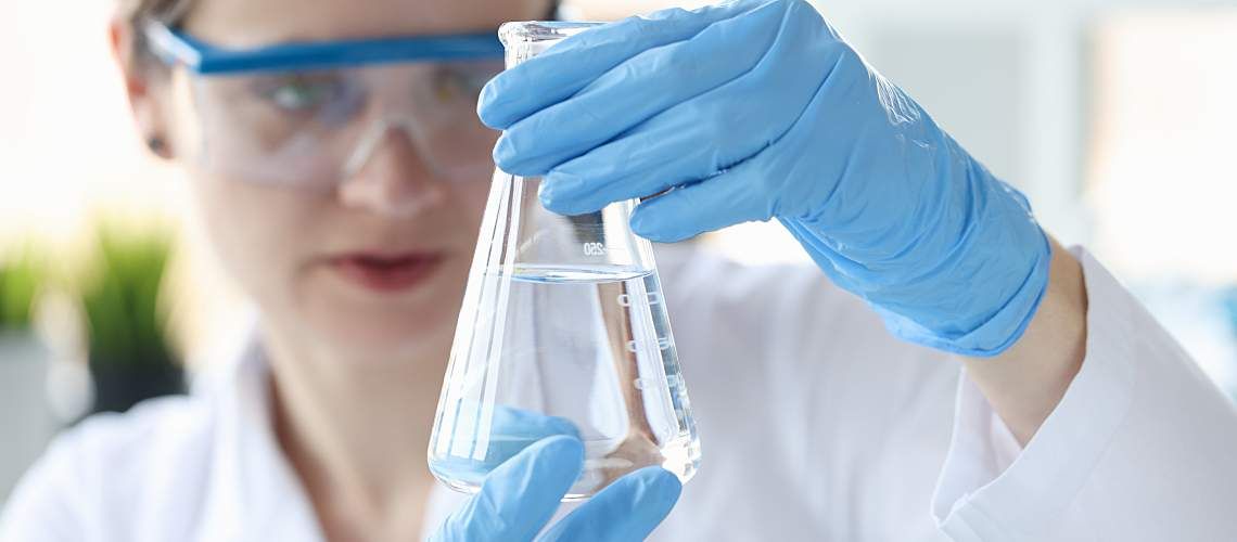 Woman scientist holding flask with transparent liquid in her hands.
