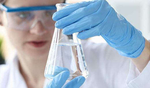 Woman scientist holding flask with transparent liquid in her hands.
