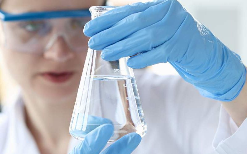 Woman scientist holding flask with transparent liquid in her hands.