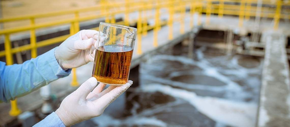 A worker holds a container of polluted water.