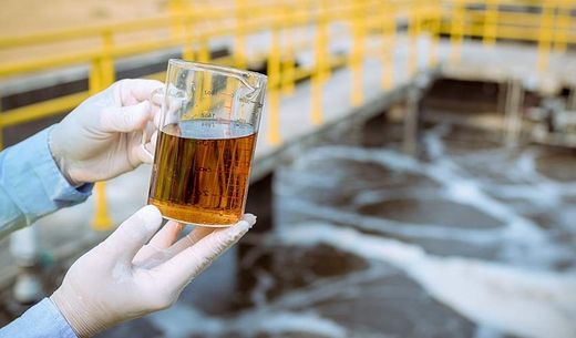 A worker holds a container of polluted water.