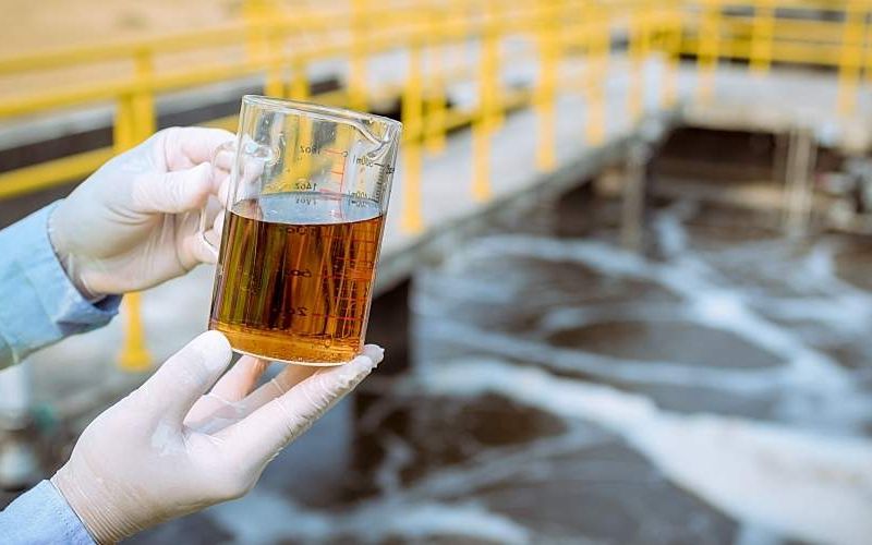 A worker holds a container of polluted water.