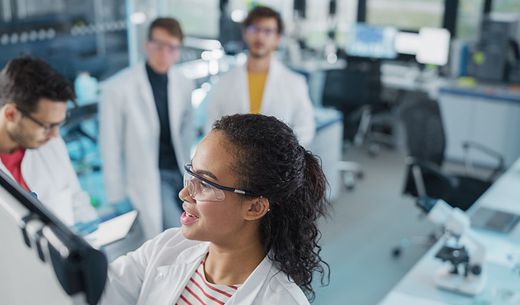 A lab team stands around a white board reviewing a work plan.