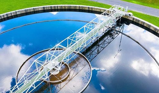 Clouds and blue sky reflected on the surface of a wastewater treatment plant clarifier.